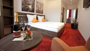 A hotel room with a bed, a bedside table with a bottle of champagne, and a small vase with flowers. - Hotel Schmidt am Markt (Meppen)