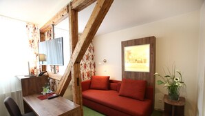 A room with a wooden desk, a red sofa, a green carpet, and a framed picture on the wall. - Hotel Schmidt am Markt (Meppen)