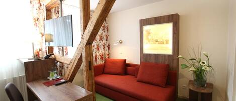 Una habitación con un escritorio de madera, un sofá rojo, una alfombra verde y un cuadro en la pared.
