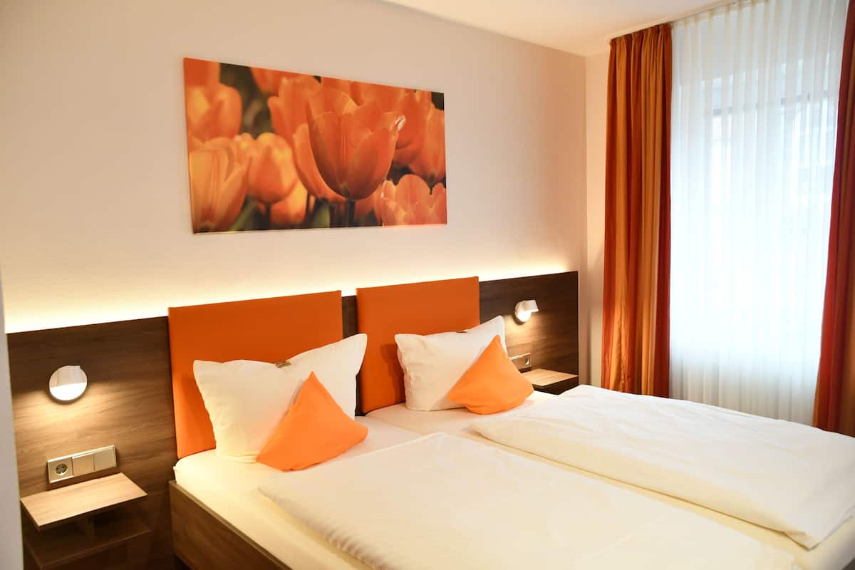 Habitación de hotel con cama doble, dos mesitas de noche, una lámpara de pared y un cuadro grande de flores.