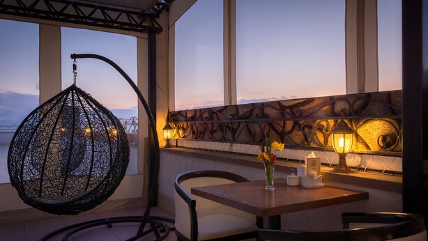 A cozy seating area with a hanging chair, a table with a vase of flowers, and a wall-mounted lamp. - 14 Floor Hotel (Yerevan)