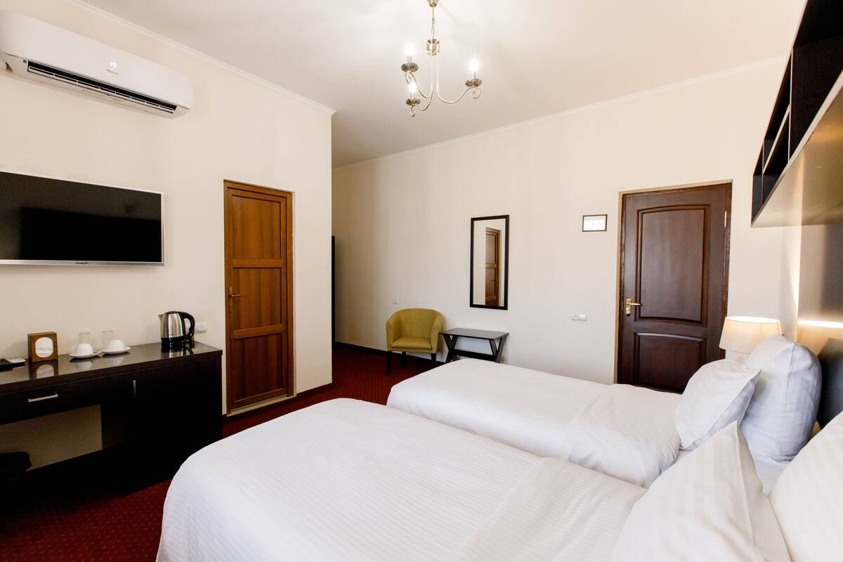 A hotel room with two beds, a desk with a coffee maker, a TV, a chair, and a wardrobe.