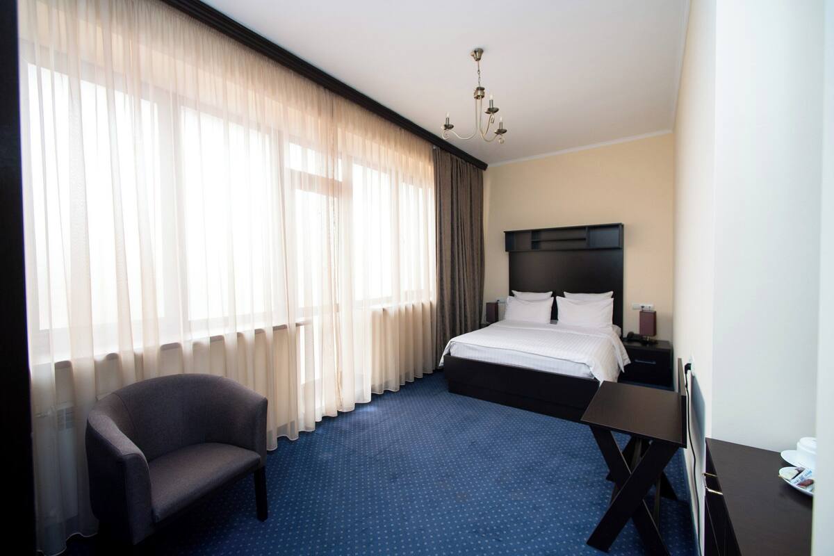 A hotel room with a bed, a chair, a desk, and a TV.
