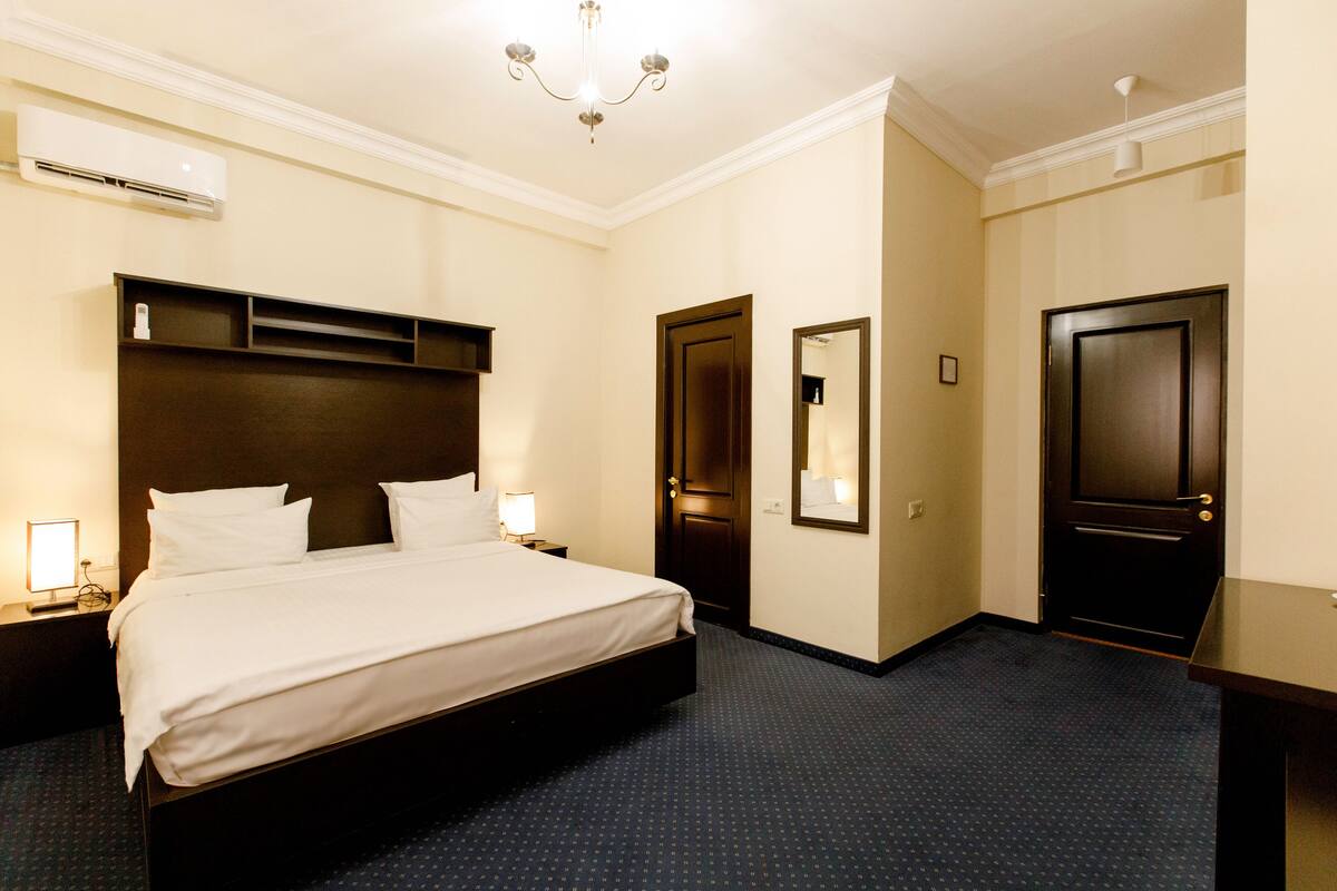 A hotel room with a large bed, a bedside table, a nightstand, a mirror, and a door.