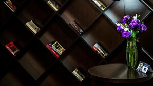 A dark wooden bookshelf with books and a vase of purple flowers on a round table. - 14 Floor Hotel (Yerevan)