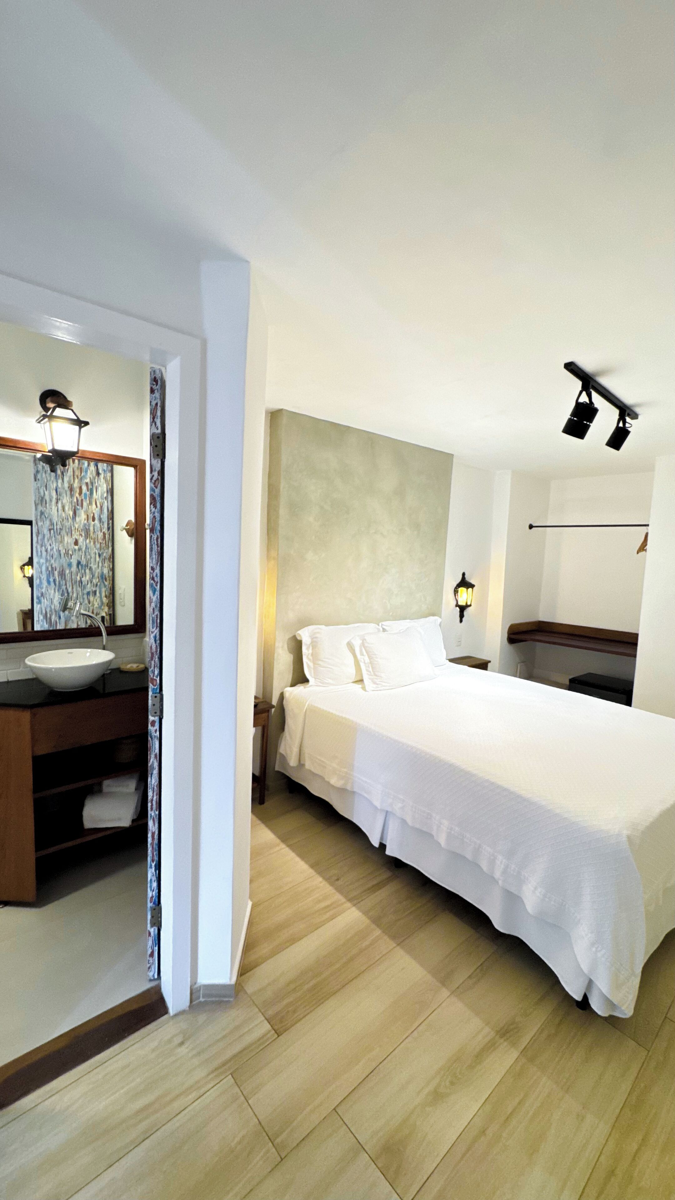 Een hotelkamer met een groot bed, een badkamer met een wastafel en spiegel, en een houten vloer.