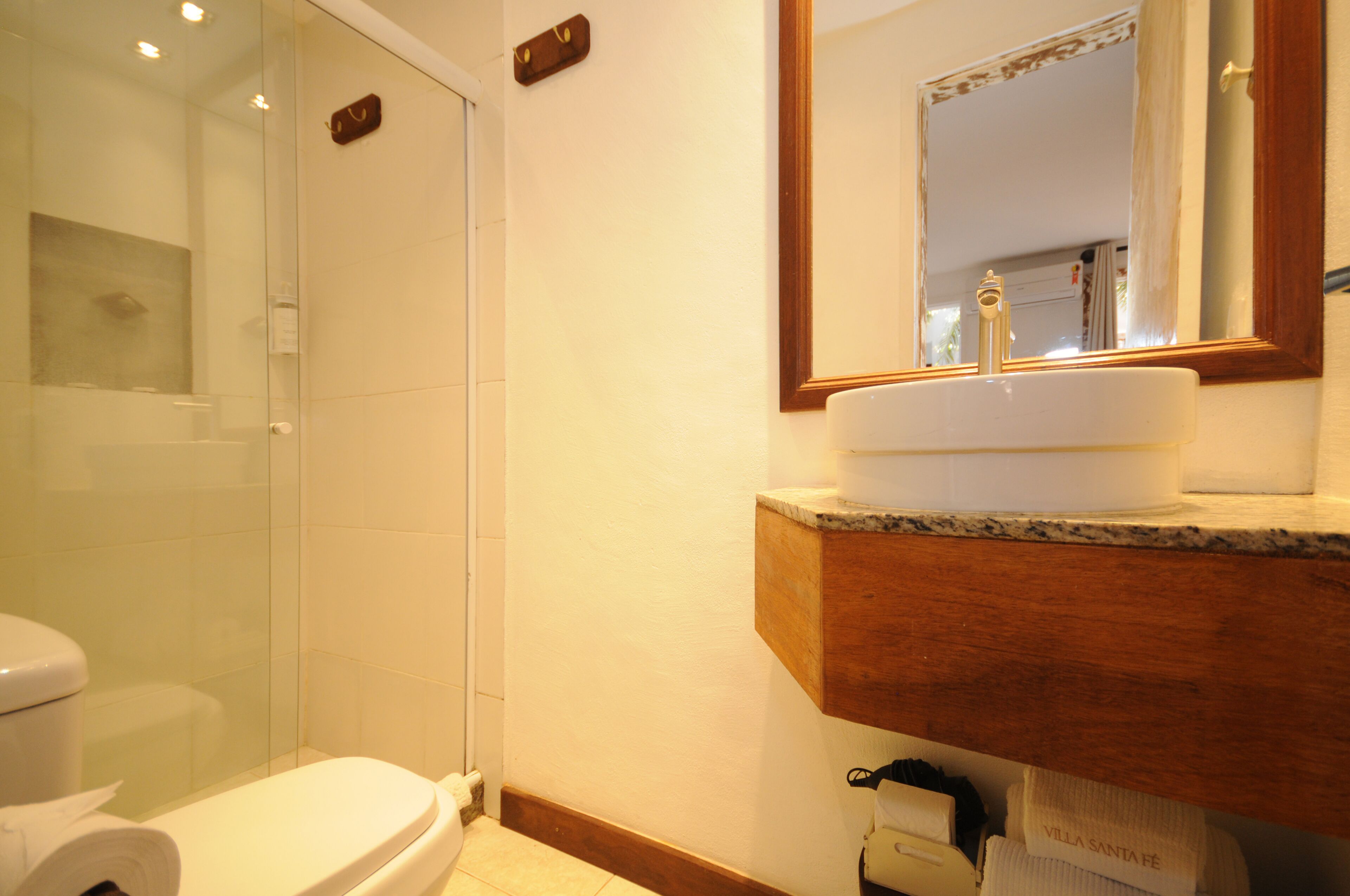 A bathroom with a toilet, a glass shower enclosure, and a sink with a wooden countertop.