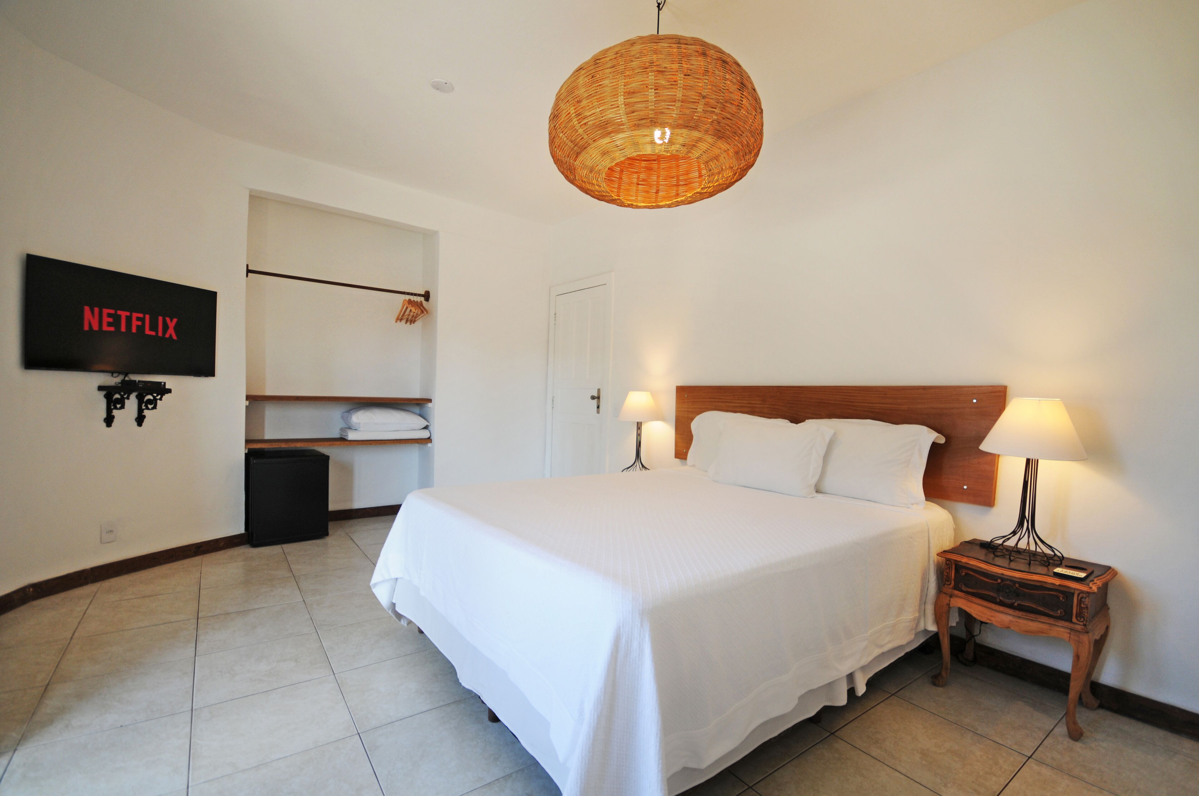 A neatly arranged hotel room with a large bed, bedside lamps, a television mounted on the wall, and a wicker ceiling light fixture.
