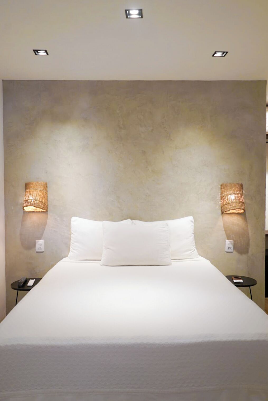 Quarto de hotel com uma cama grande, duas luminárias de cabeceira e uma parede com textura.