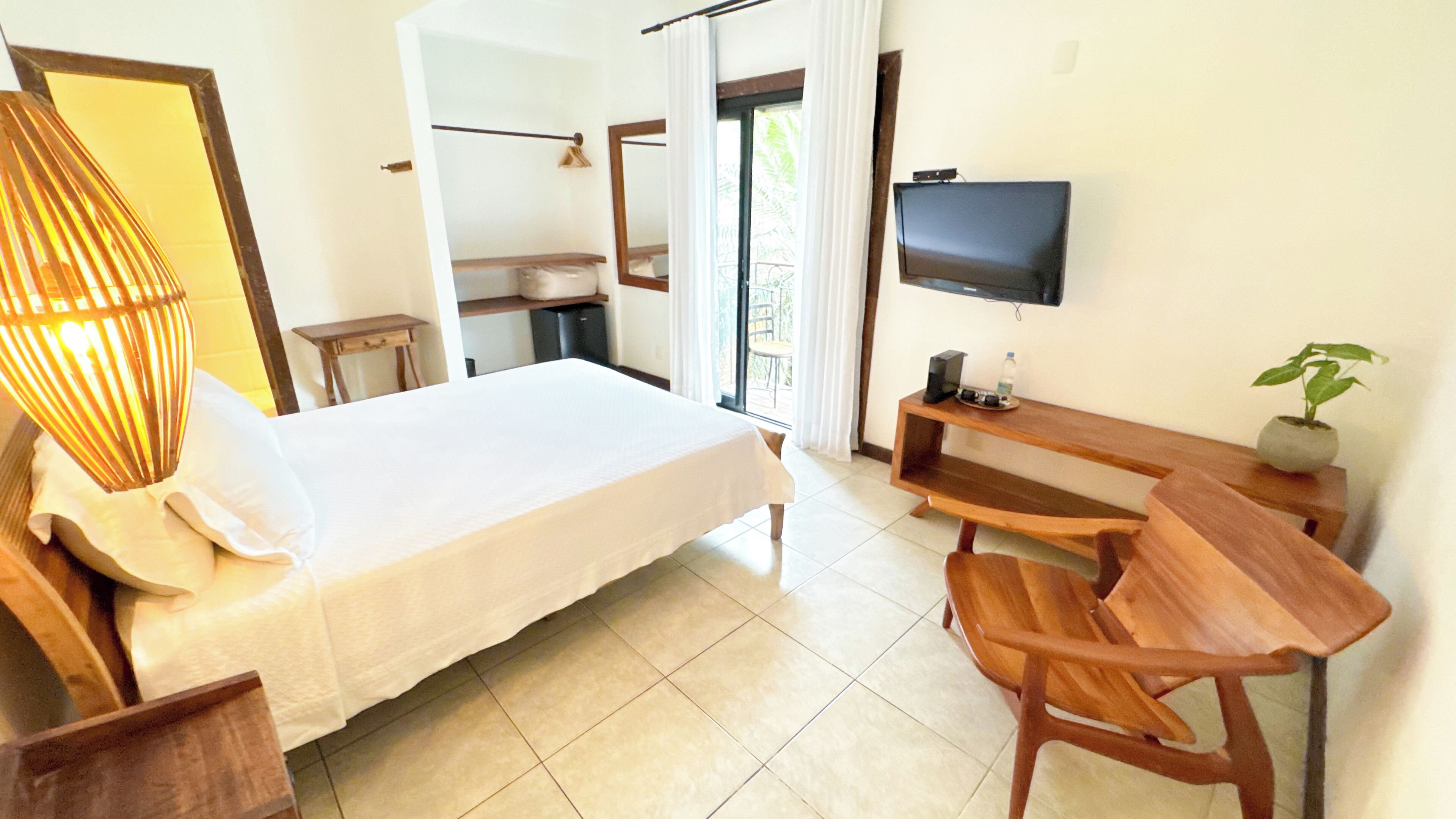 A hotel room with a bed, a desk with a chair, a television, and a potted plant.