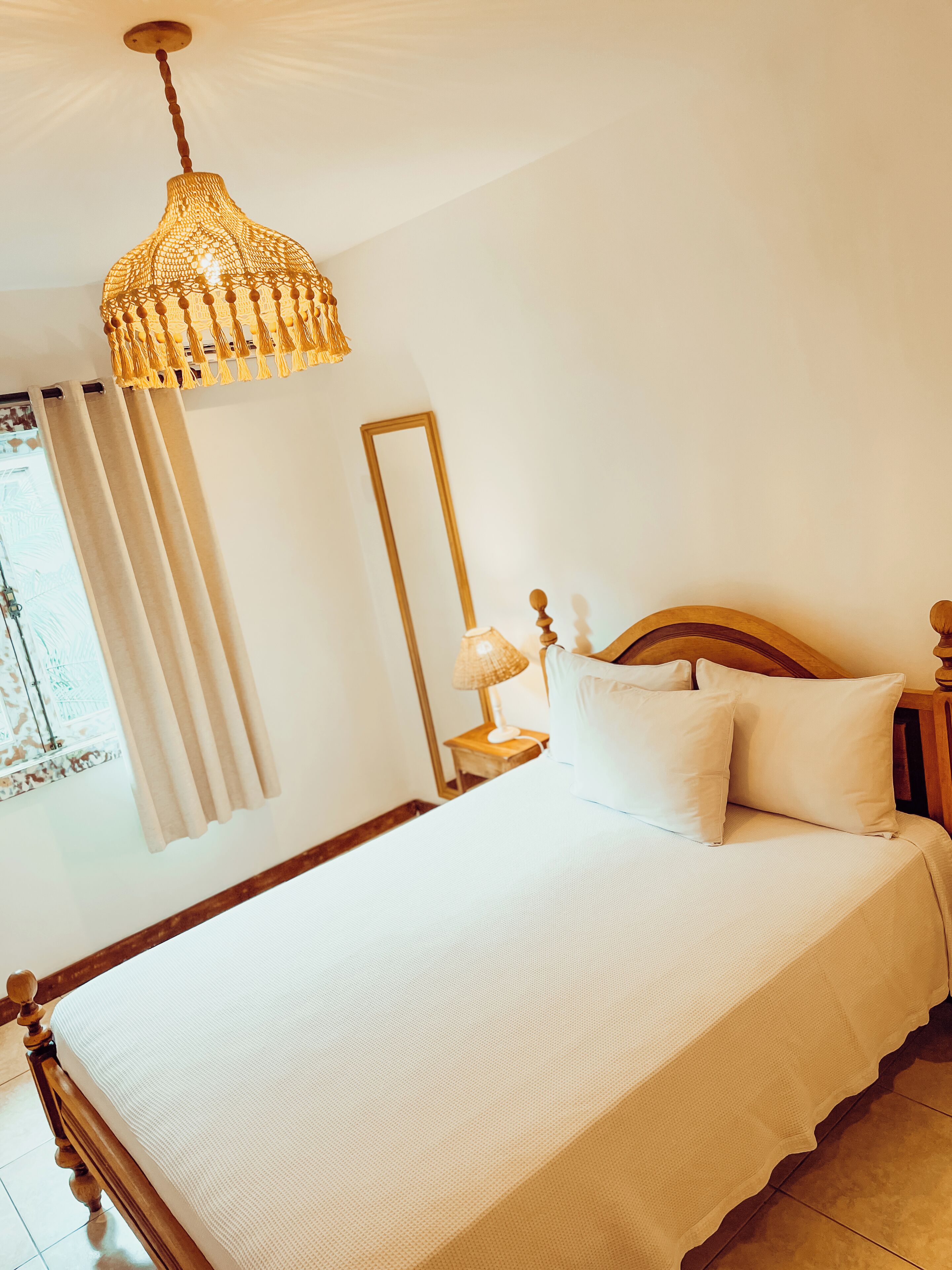 A neatly made bed with white linens, a wooden headboard, and a hanging light fixture.