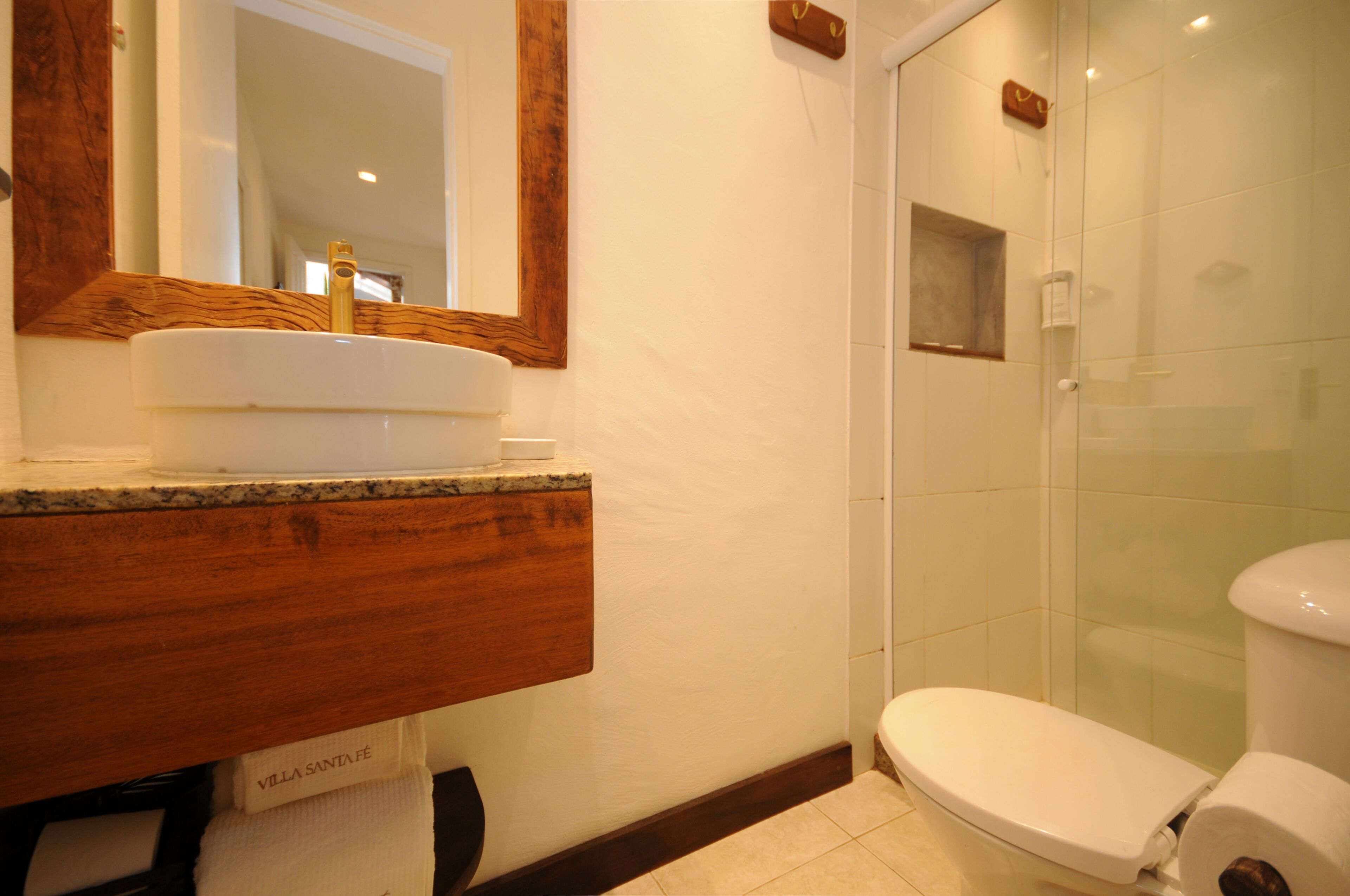 Ett badrum med ett handfat i trä, en vit tvättställ, en spegel och en duschkabin med glasväggar.