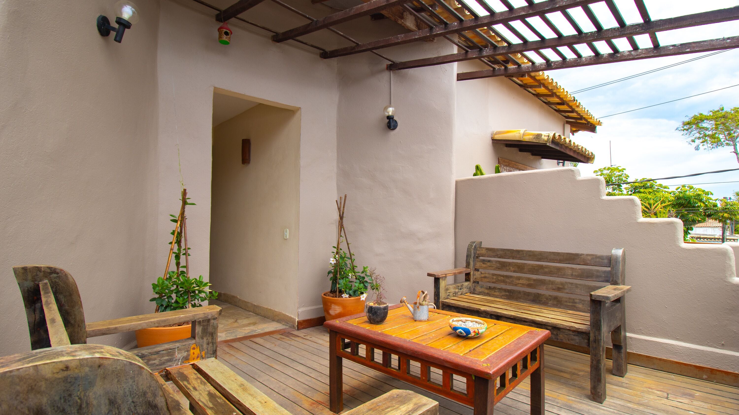Une terrasse en bois avec un banc et une table, des plantes en pot et une structure en forme de pergola.