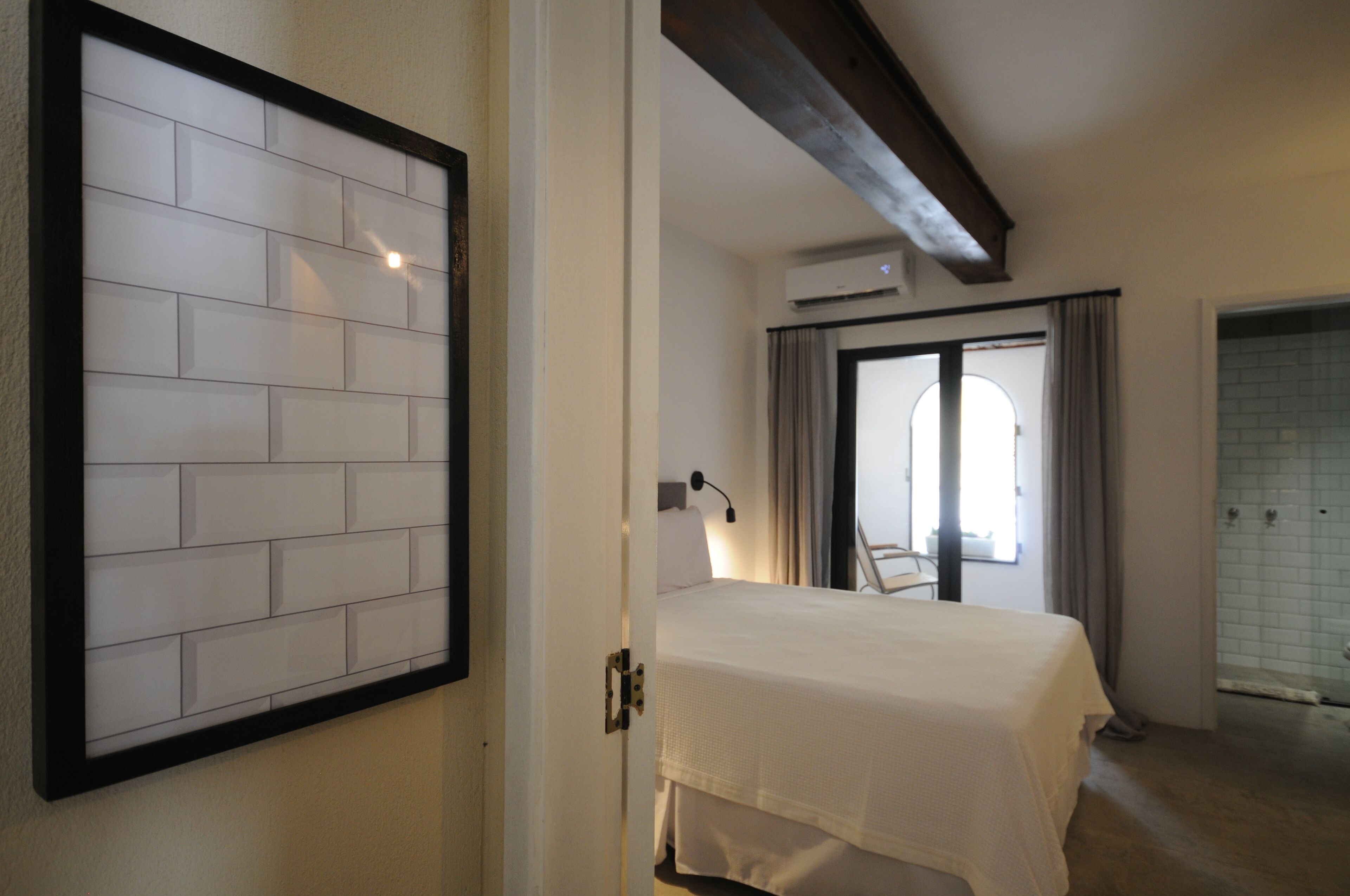 Een slaapkamer met een bed, een witte muur met een ingelijst kunstwerk, een plafondventilator en een raam met gordijnen.