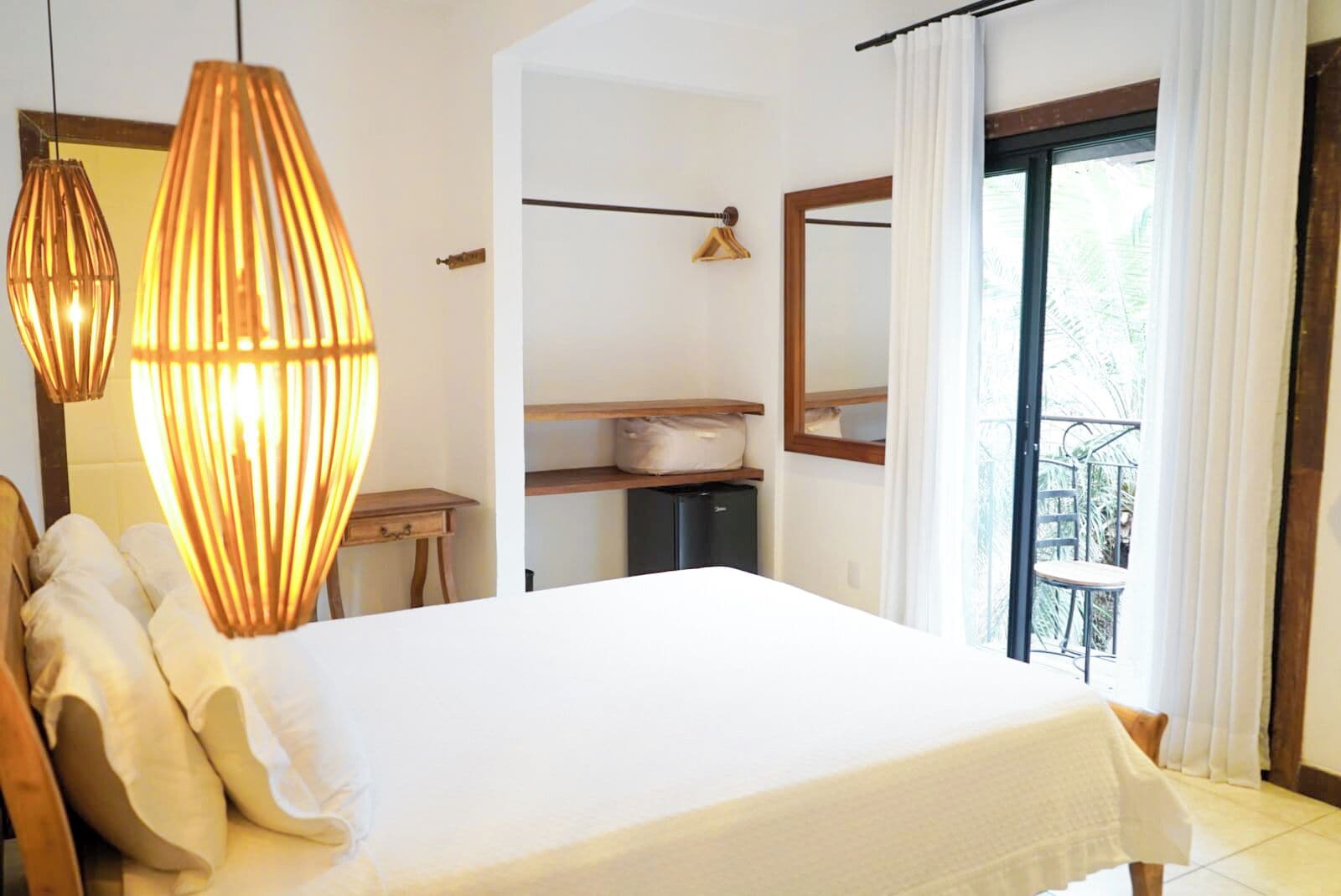 A bedroom with a bed, bedside tables, a dresser, a mirror, and a balcony with a view.