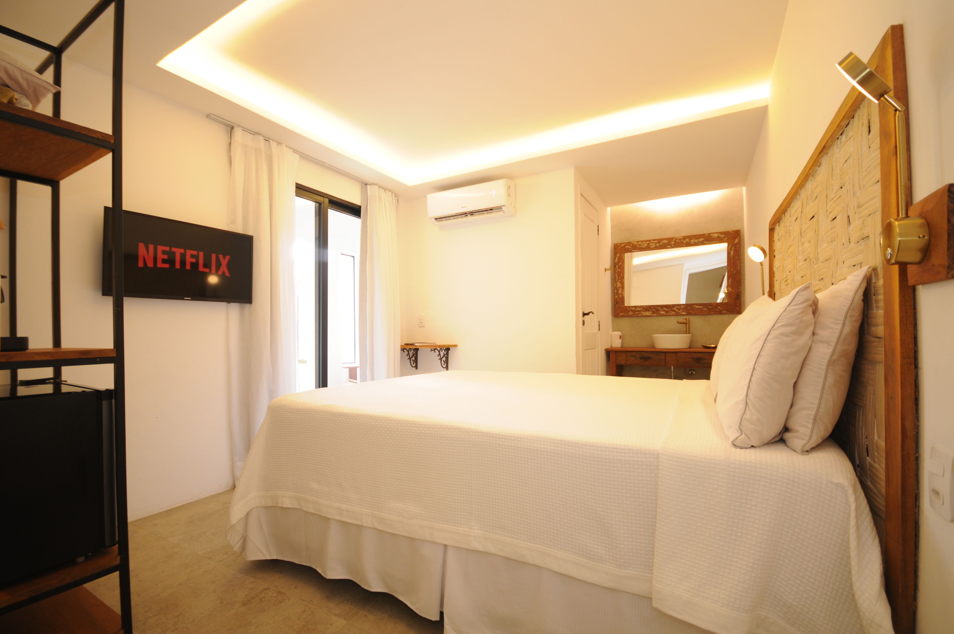 Een hotelkamer met een bed, een aan de muur bevestigde televisie, een airconditioning, een nachtkastje en een spiegel.