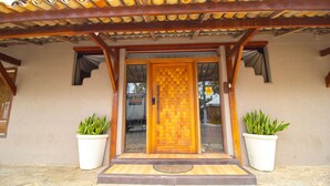 Une porte en bois ornée d’un motif décoratif, flanquée de deux plantes en pot.
