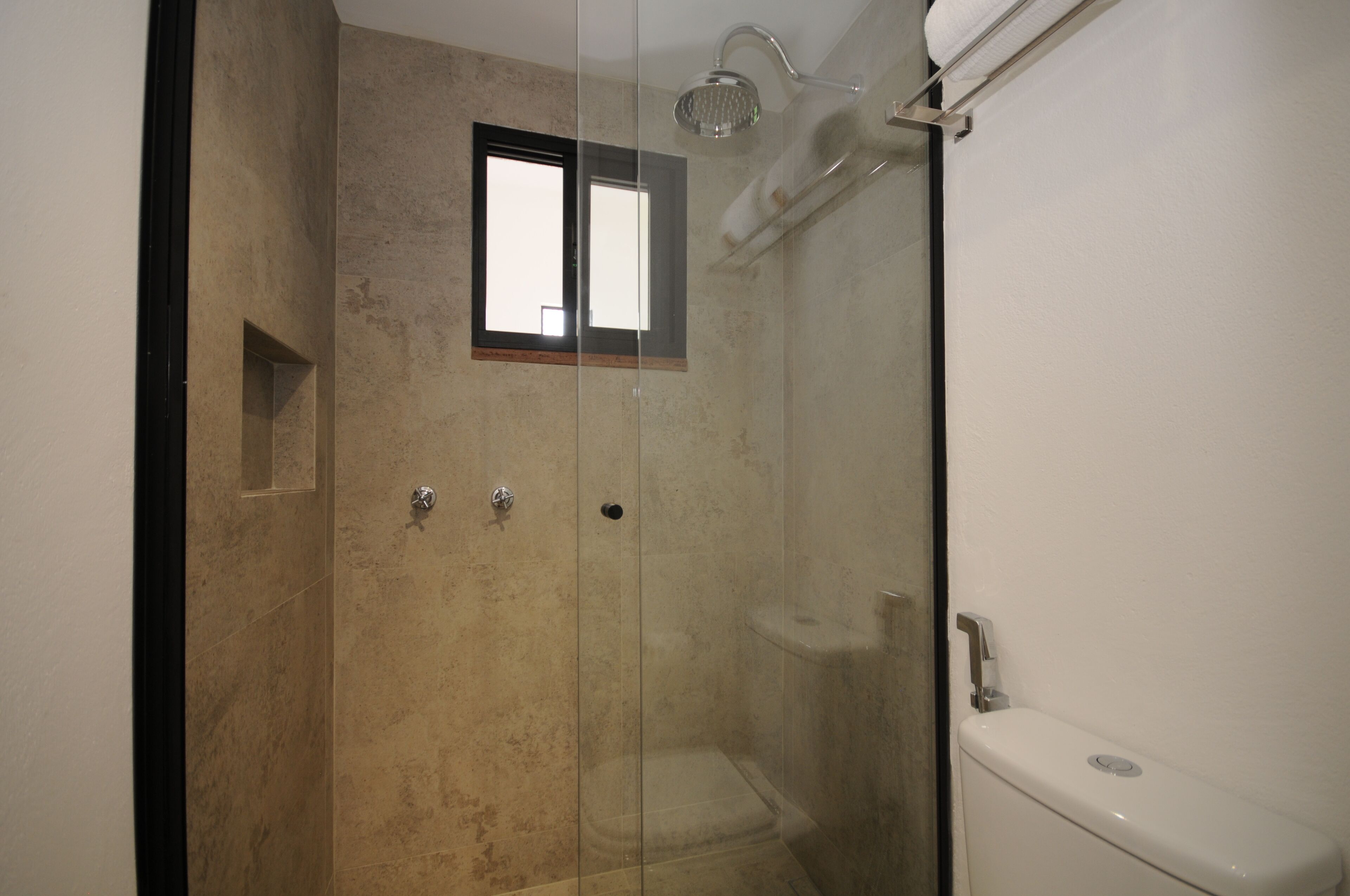 A bathroom with a glass-enclosed shower, a toilet, and a small window.