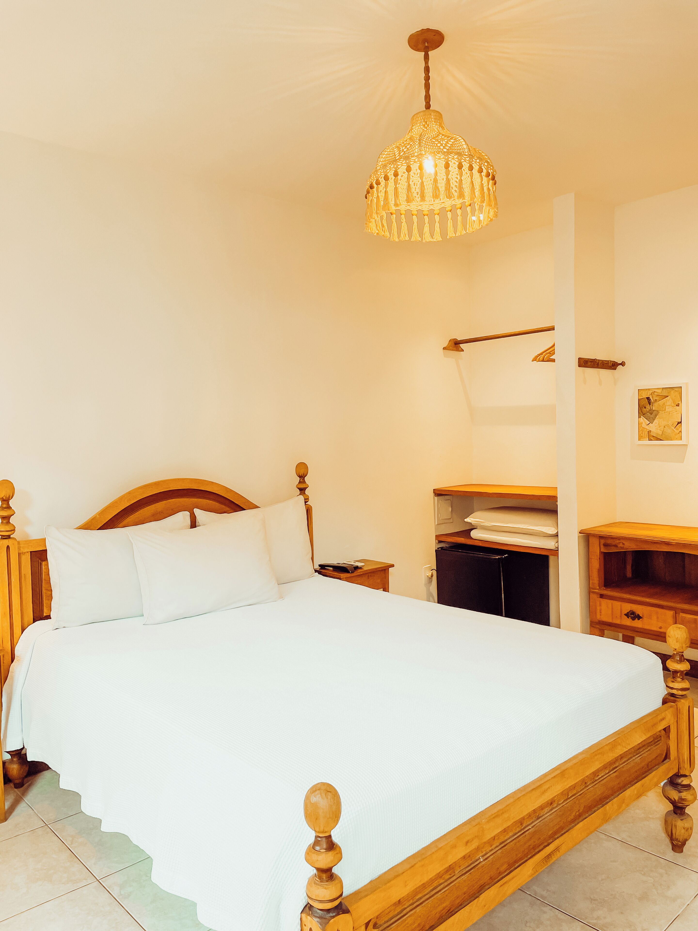 A neatly made bed with a wooden headboard, a bedside table, a nightstand, and a hanging light fixture.