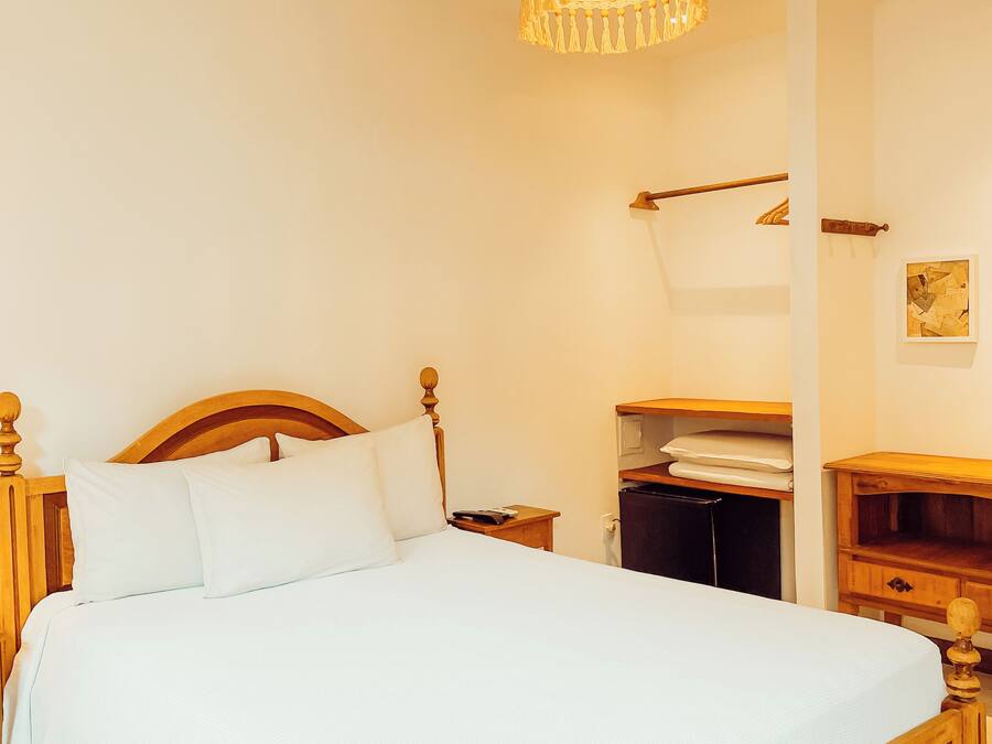 A neatly made bed with a wooden headboard, a bedside table, a nightstand, and a hanging light fixture.