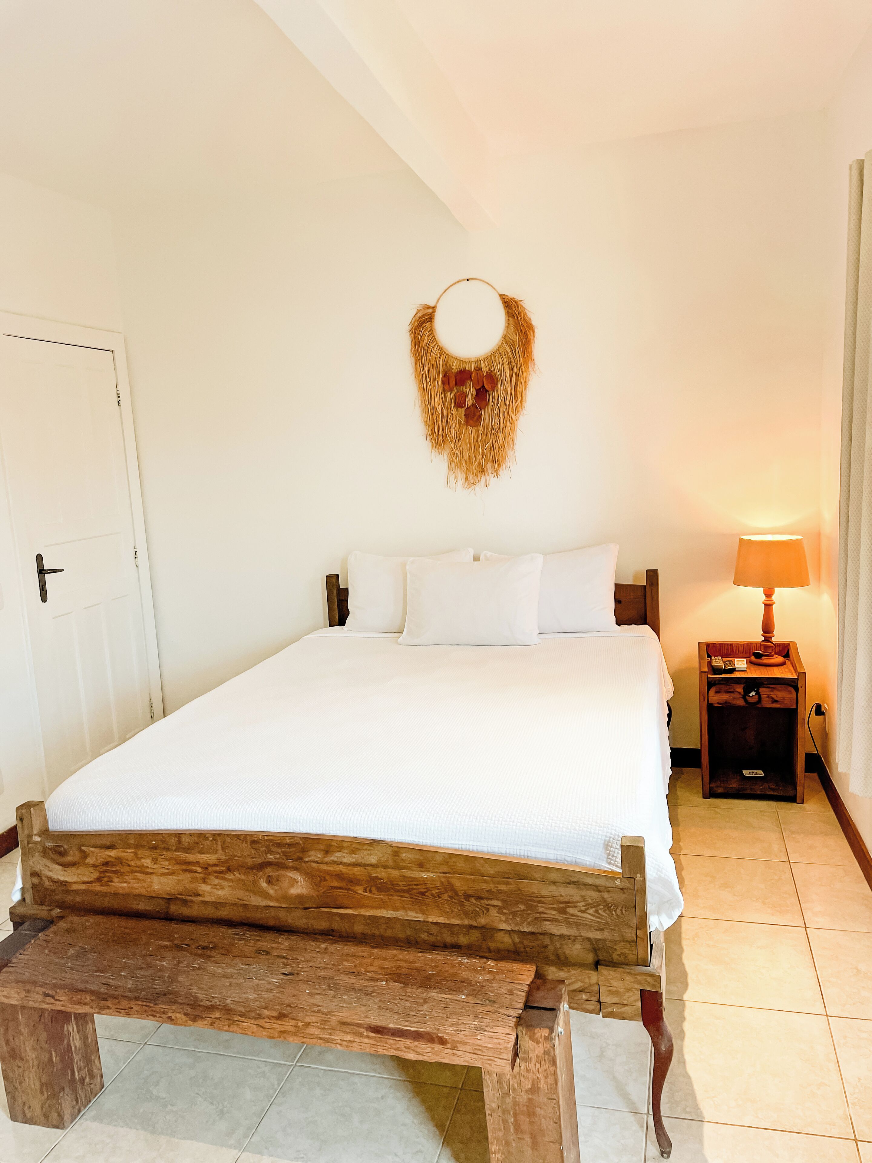 A bed with a wooden headboard, a bedside table with a lamp, and a wall-mounted decorative item.