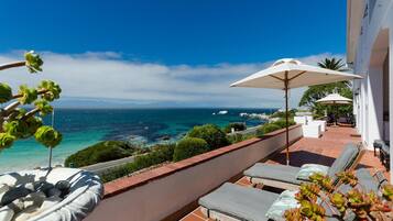 A balcony with lounge chairs and umbrellas overlooking a coastal view.