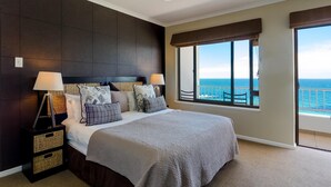 A spacious bedroom with a large bed, two bedside tables with lamps, a view of the ocean through a large window, and a balcony with a railing. - Whale View Manor Guesthouse (Cape Town)
