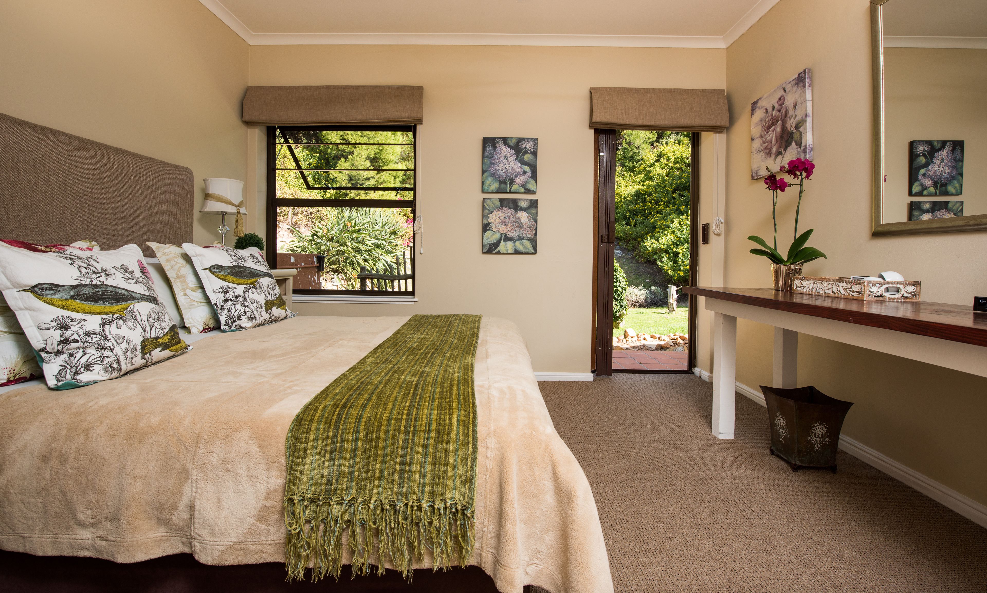 A bedroom with a bed, a bedside table, a mirror, and a window with a view of greenery.