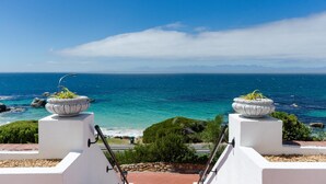 A coastal view with two planters on a white structure, overlooking the sea and distant mountains. - Whale View Manor Guesthouse (Cape Town)