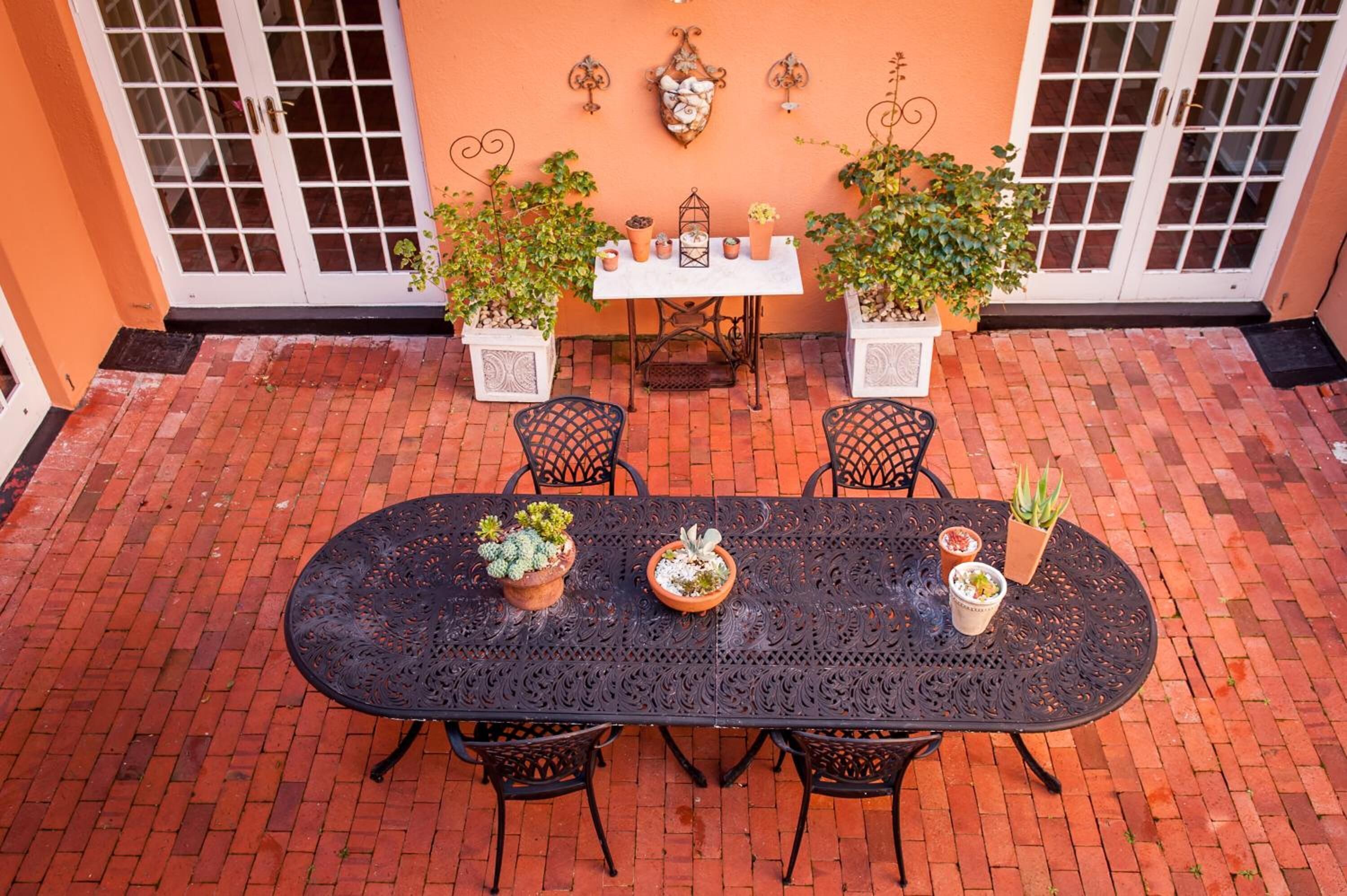 A patio with a black wrought iron table and chairs, surrounded by potted plants and a white door.