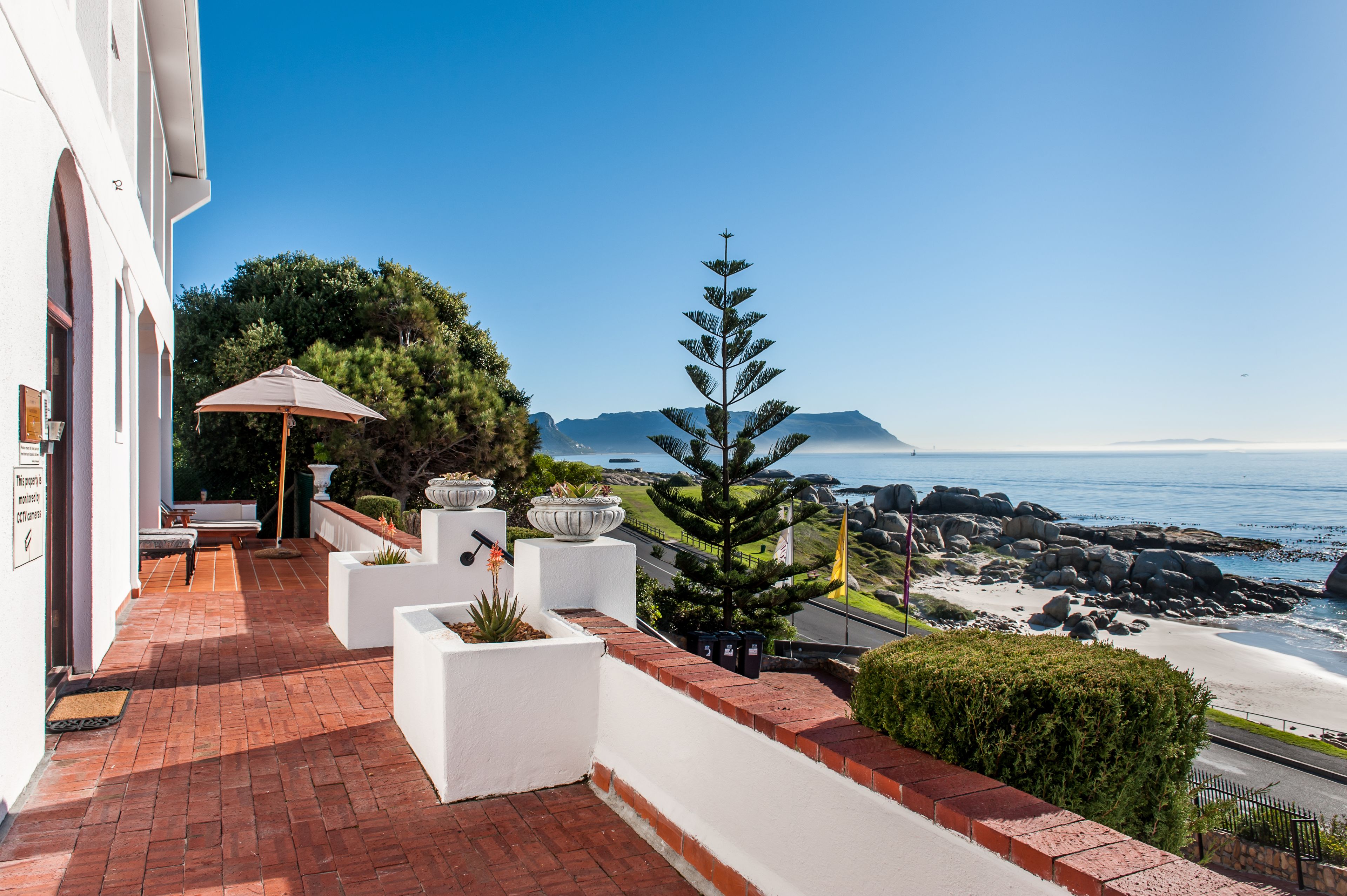 A patio with outdoor seating, a large umbrella, and a view of the ocean and mountains.