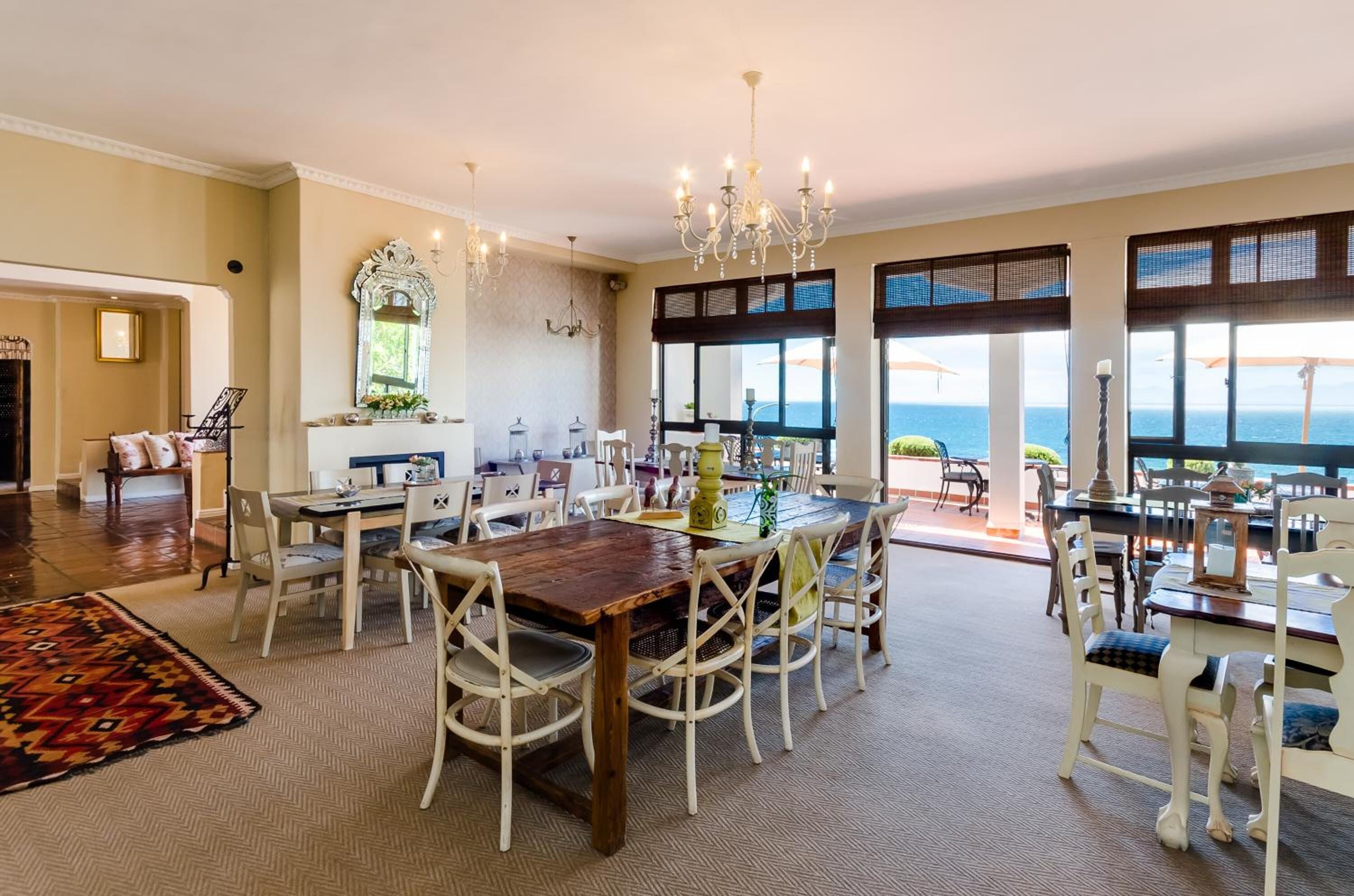 A spacious dining area with a large wooden table and white wicker chairs, overlooking a scenic ocean view through large windows.