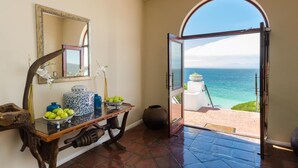 A room with a view of the ocean through an open door, a mirror on the wall, and a table with decorative items. - Whale View Manor Guesthouse (Cape Town)