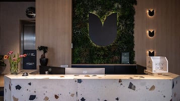 Un mostrador de recepción con encimera de terrazo, una planta grande colgada en la pared y un buzón para llaves.