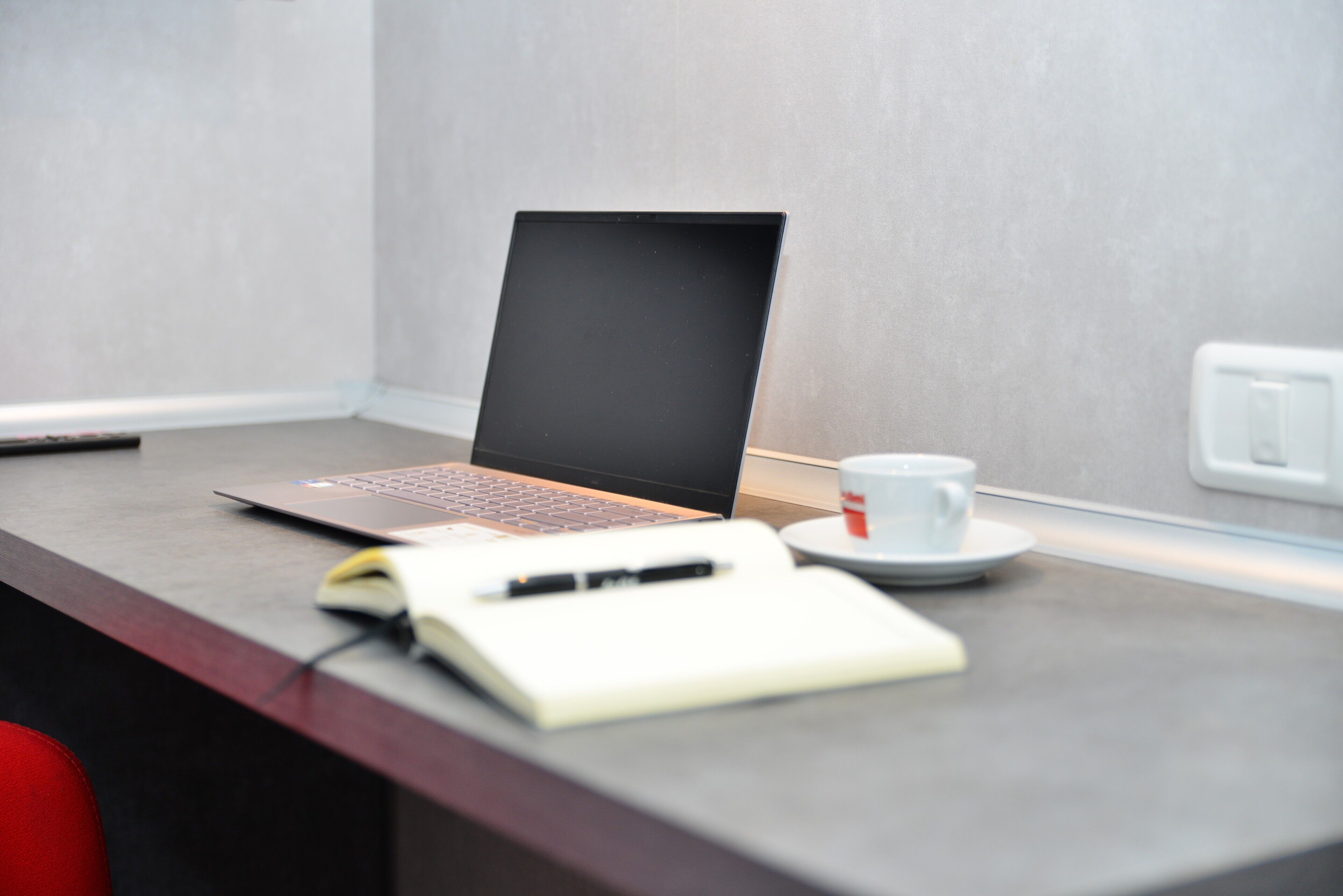 A laptop on a desk with a notebook, pen, and a cup of coffee.