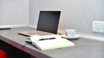 A laptop on a desk with a notebook, pen, and a cup of coffee.