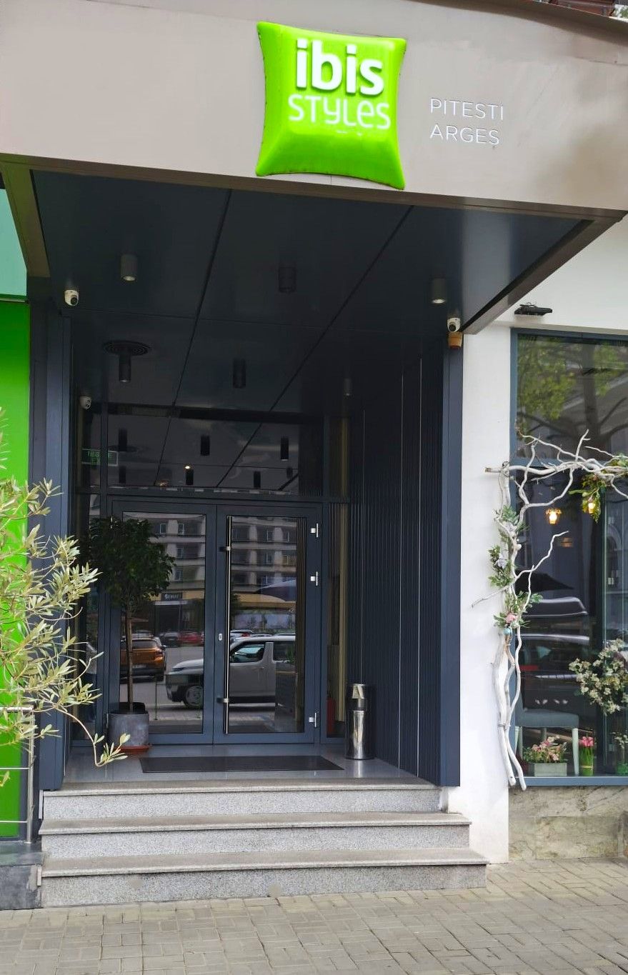 Une entrée d'immeuble avec une enseigne verte indiquant « ibis Styles » et un escalier menant à la porte.