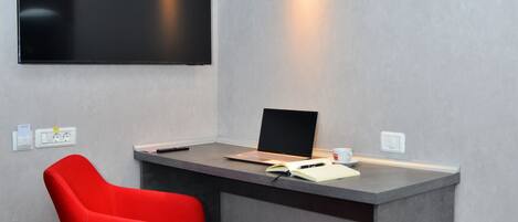 Habitación de hotel moderna con escritorio, una silla roja, un televisor de pantalla plana y una lámpara de pared.