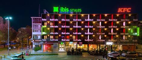 Ein mehrstöckiges Hotel mit KFC- und ibis-Beschilderung, Balkonen und einem Parkplatz.