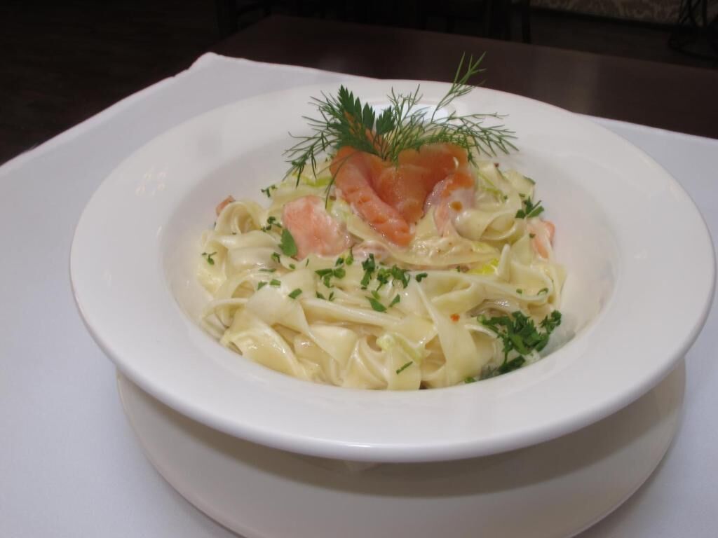 A white plate with a dish of pasta garnished with herbs and salmon.