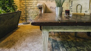 A rustic wooden table with a metal bucket, a potted plant, a floor lamp, and a menu stand against a brick wall. - CitiHotel Veliki (Novi Sad)