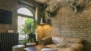 A cozy interior with exposed brick walls, a leather couch with 'NOWN GROBE' branding, a wooden table, and hanging pendant lights. - CitiHotel Veliki (Novi Sad)