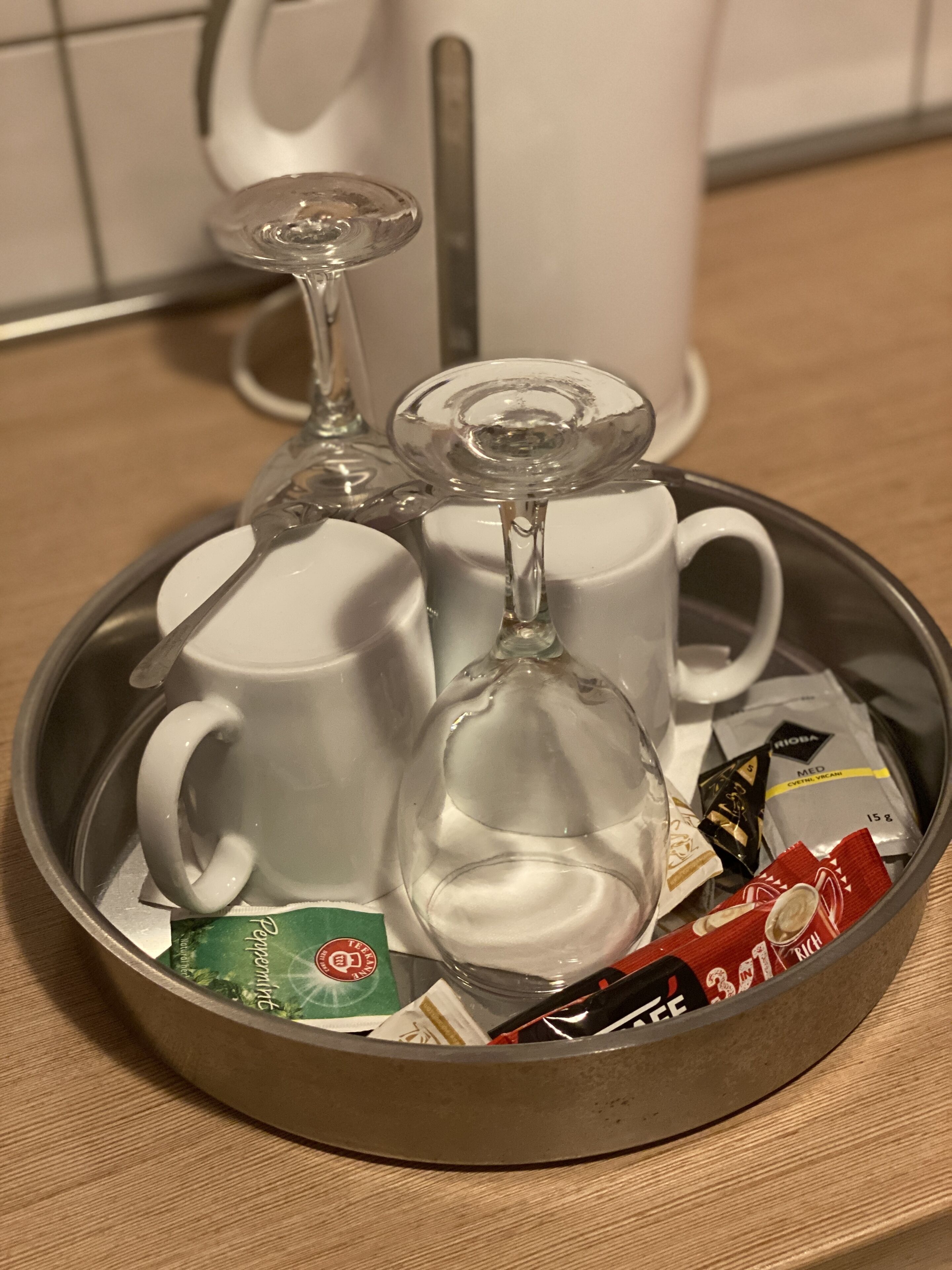 A tray with two white mugs, a glass, and various packaged items.