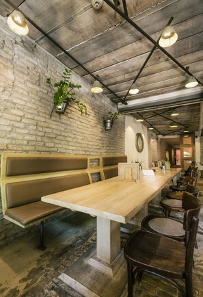 A restaurant with a long wooden table, multiple seating options including benches and chairs, a brick wall, and hanging pendant lights. - CitiHotel Veliki (Novi Sad)