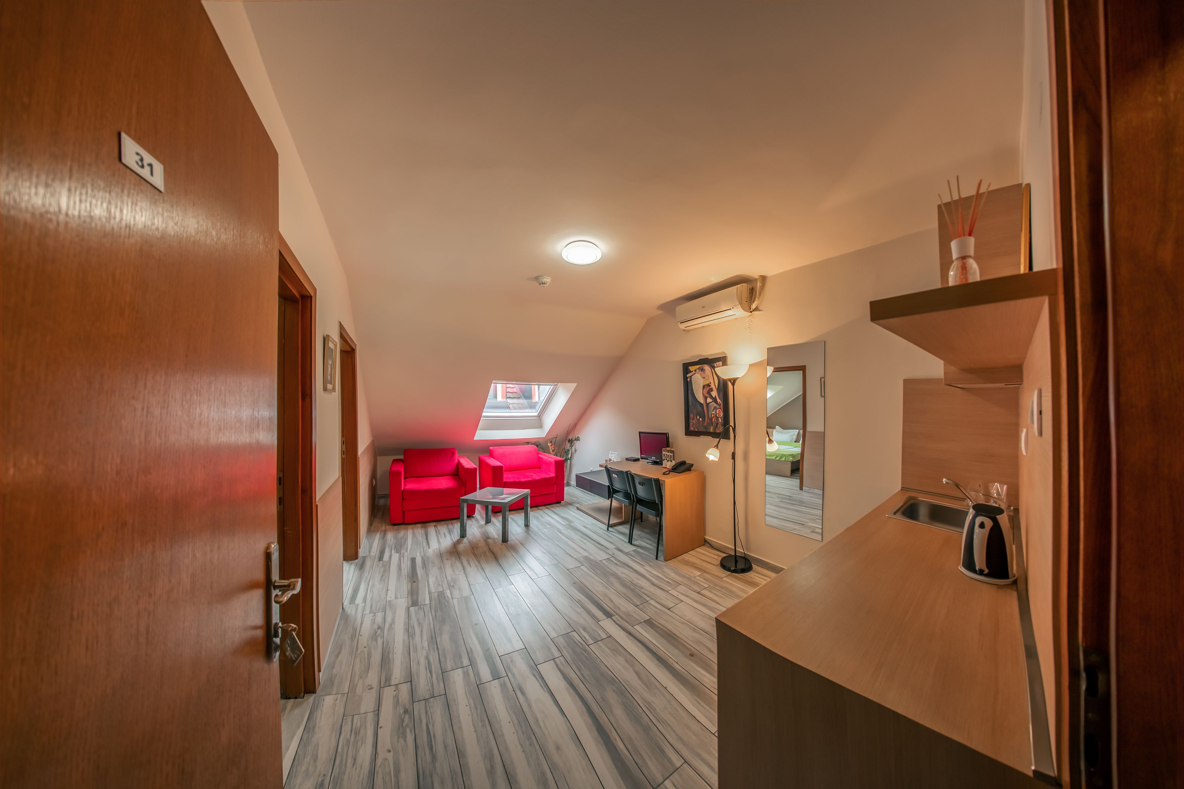 A modern apartment with a kitchen, a dining area with red chairs, a small table, and a skylight.