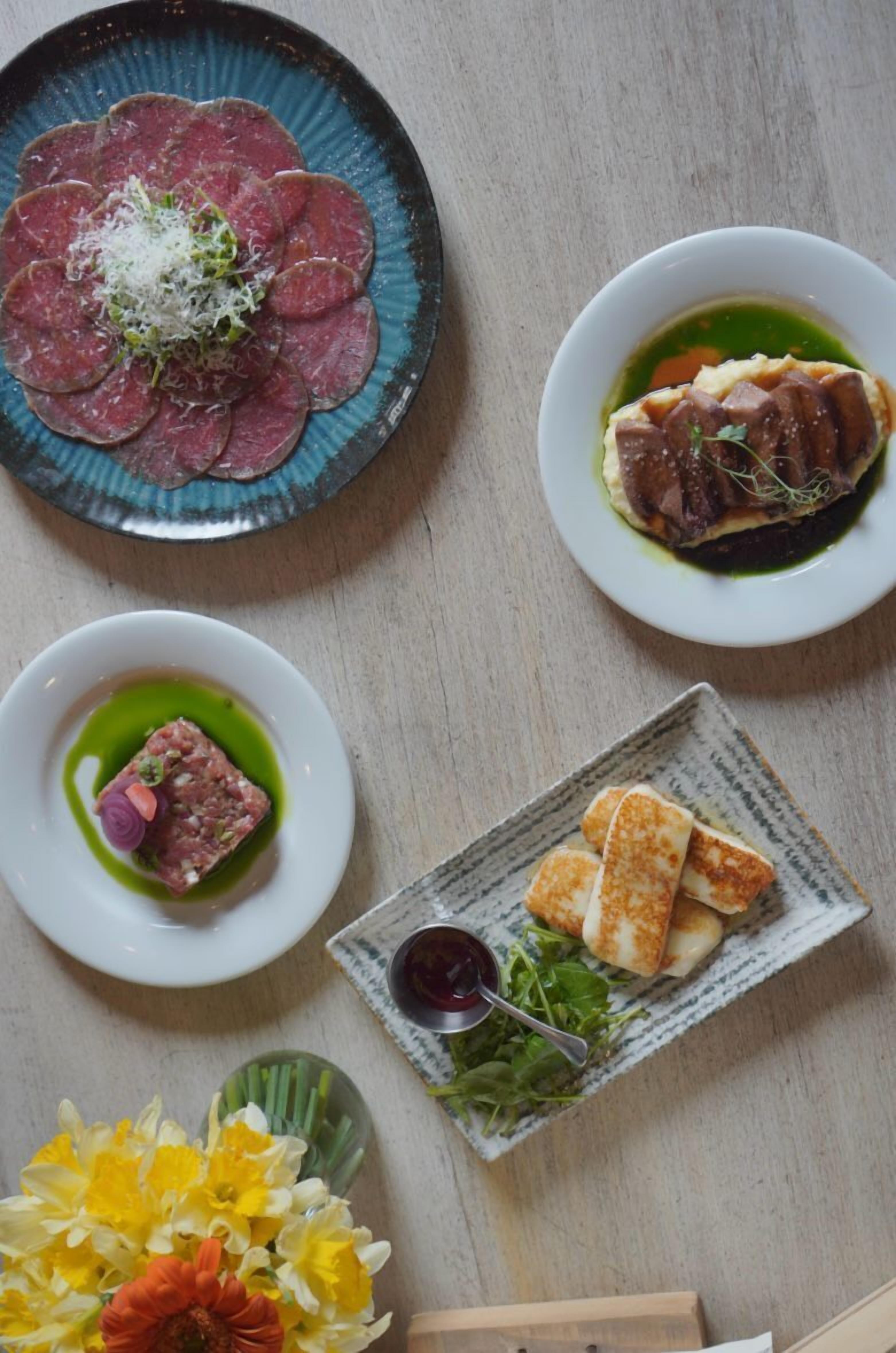A table with various dishes including a plate of sliced meat, a bowl of soup, and a plate of cheese and crackers.
