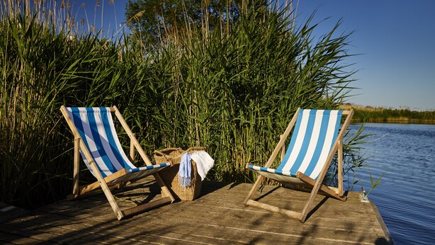 Two striped beach chairs on a wooden dock by a body of water with tall grasses and trees in the background. - Kurort Stara Wędzarnia (Gdansk)