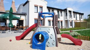 A playground with a slide and climbing structure, set against a building with multiple windows and a balcony. - Kurort Stara Wędzarnia (Gdansk)