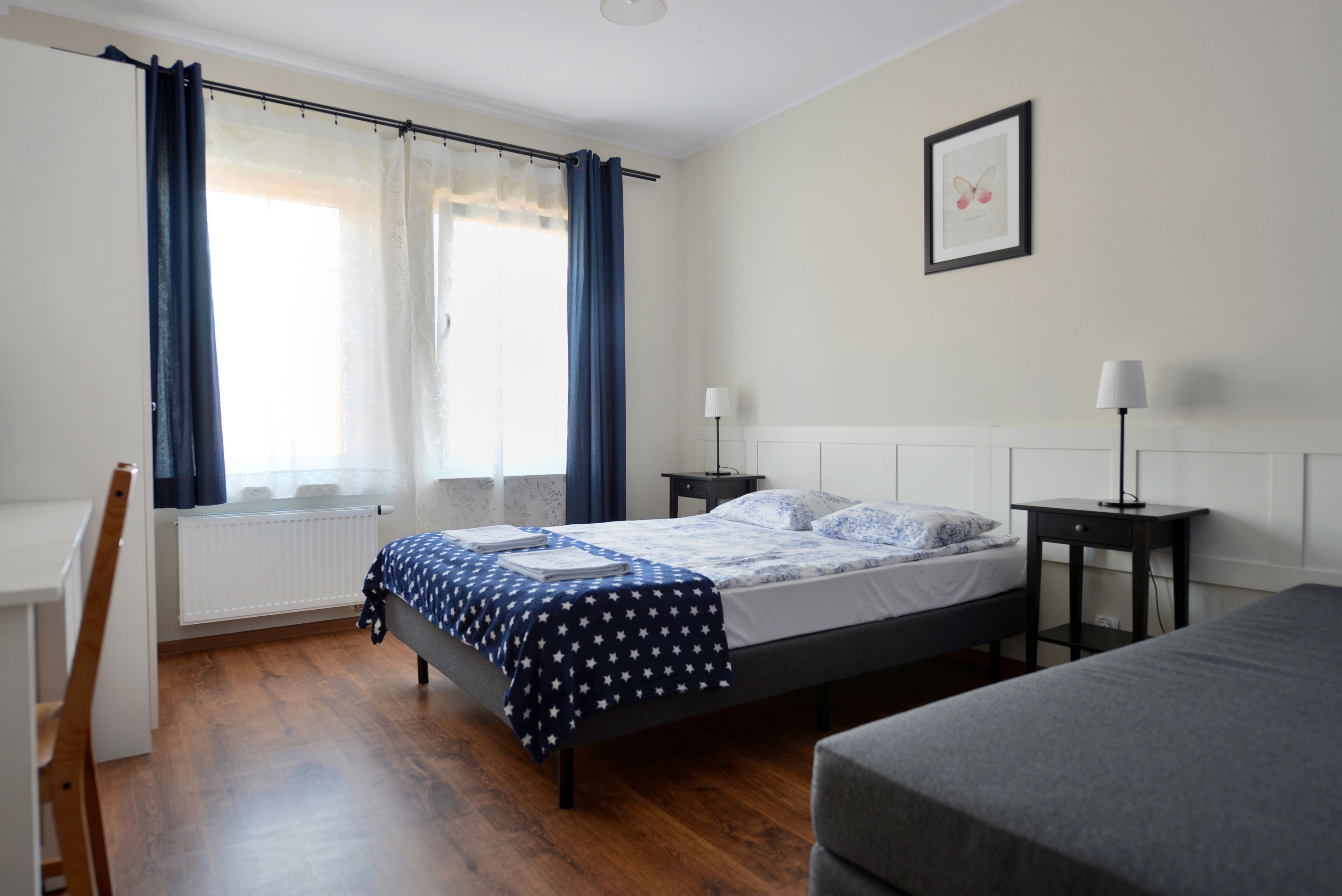 A bedroom with a bed, a chair, a nightstand, a lamp, and a window with curtains.