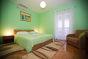 Un dormitorio con cama, mesita de noche, sofá, ventana con cortinas y un cuadro en la pared.